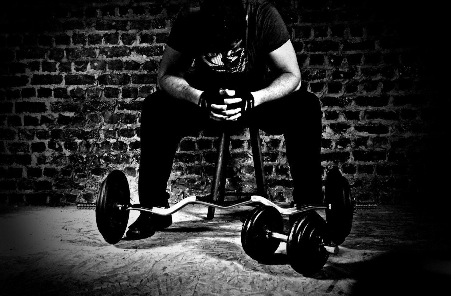 black and white of man on stool leaning over barbell and weights